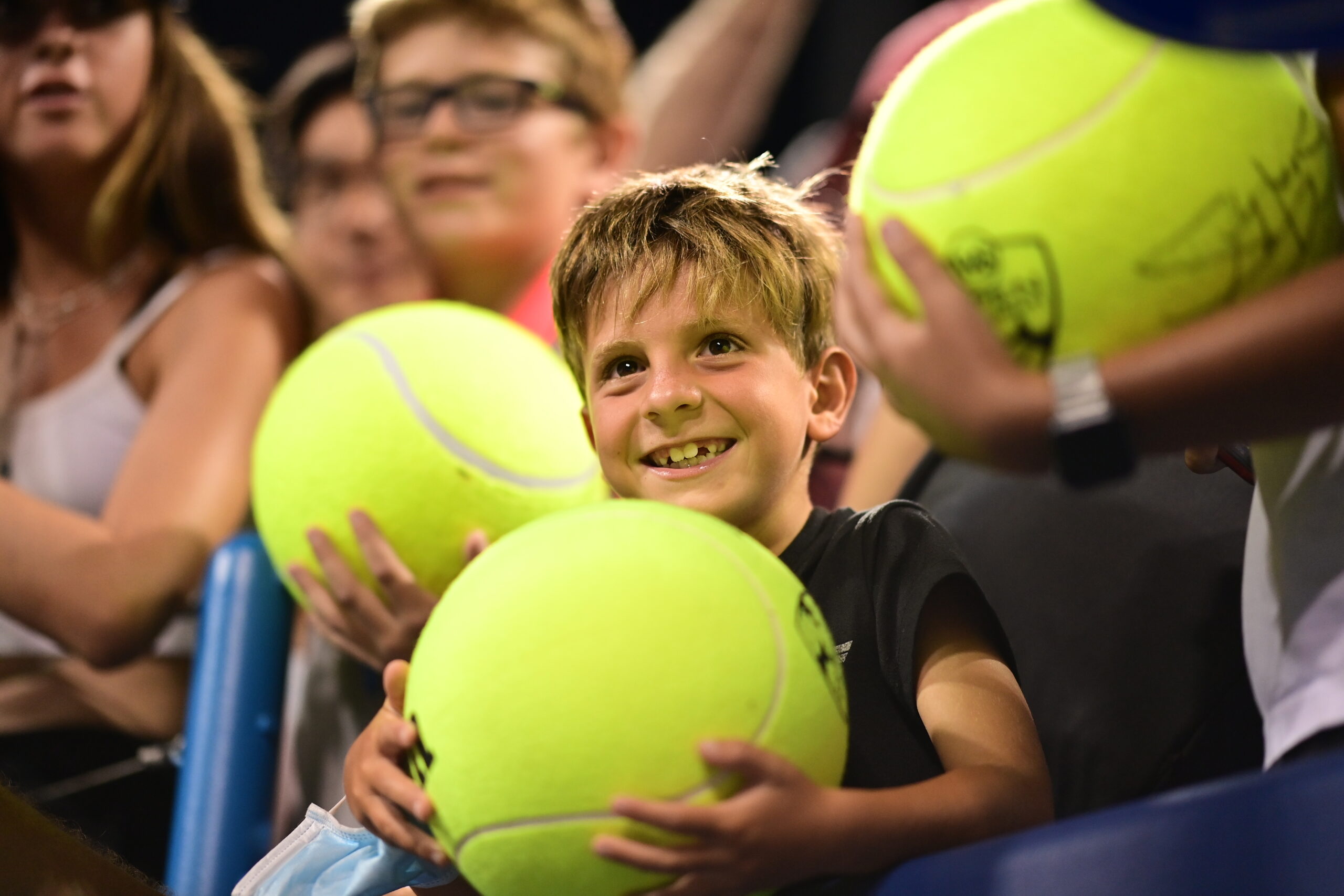 A child holding a large novelty tennis ball and smiling