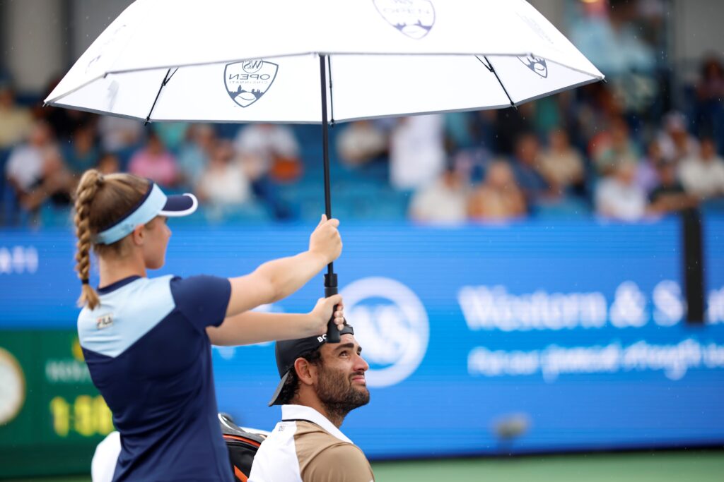 Ballperson holds an umbrella over Matteo Berretinni