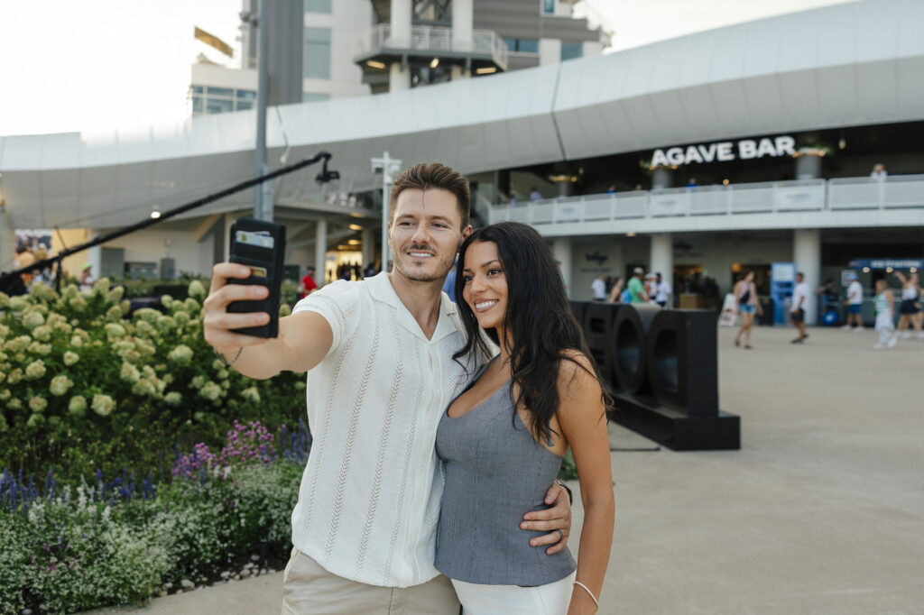 A couple takes a selfie near the Agave Bar. He wears a cream pointelle knit camp-collar shirt with tan trousers, and she wears a grey pinstripe halter top with white trousers.