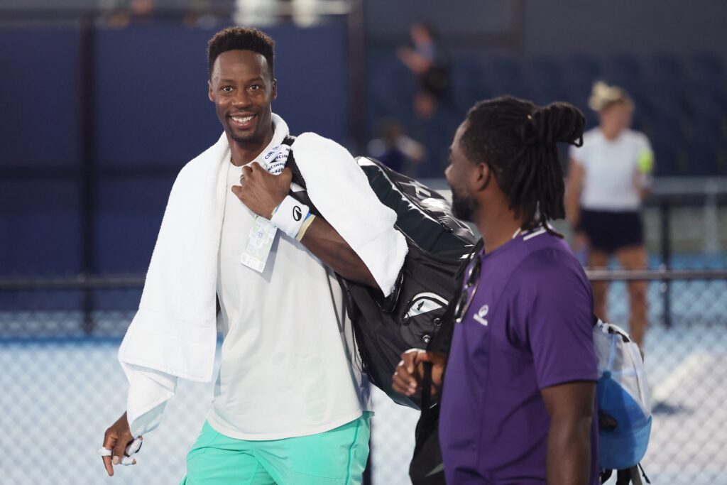 Monfils walking across the court and smiling at the camera with a towel around his neck