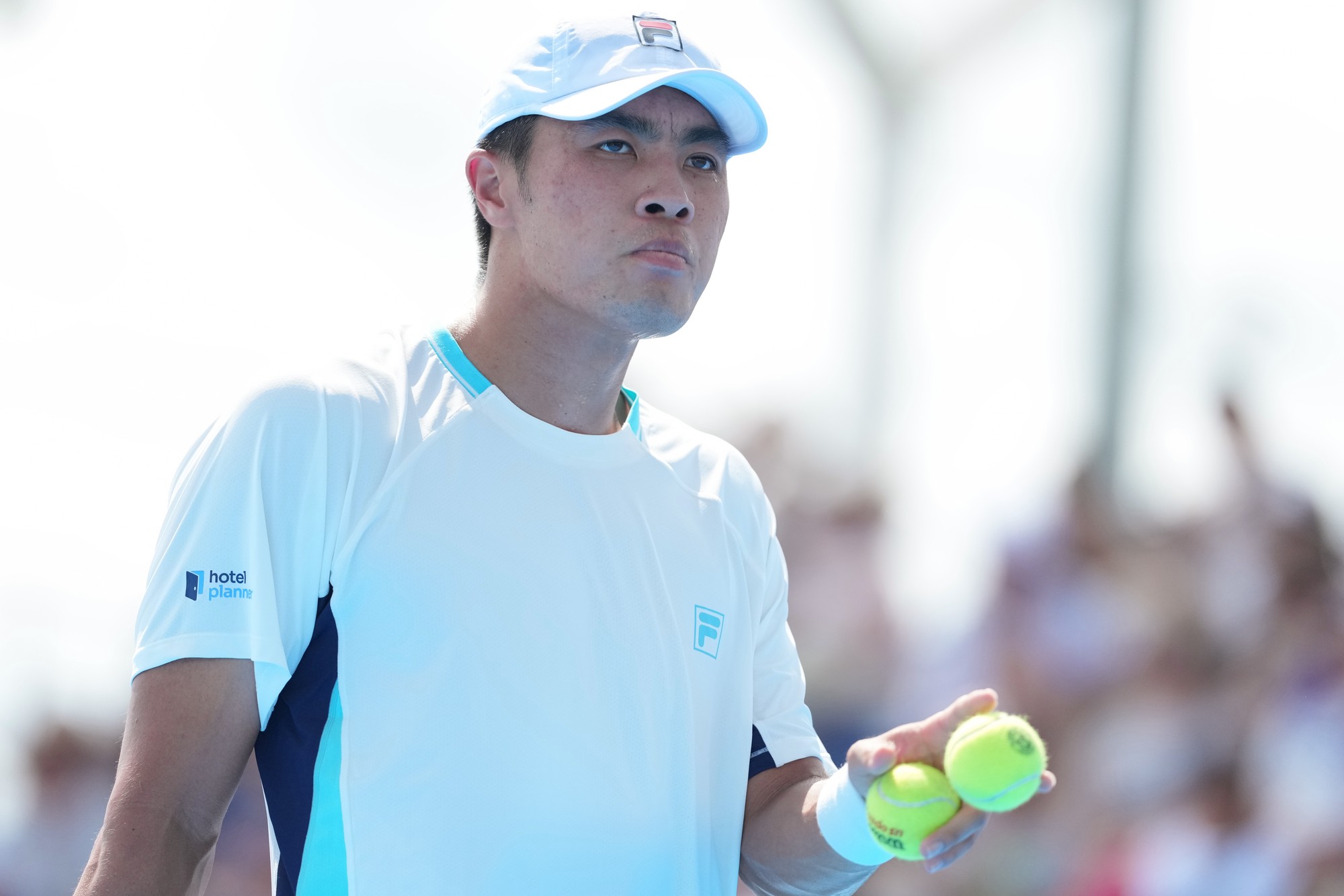 A determined looking tennis player holding a tennis ball with a blurred crowd in the background