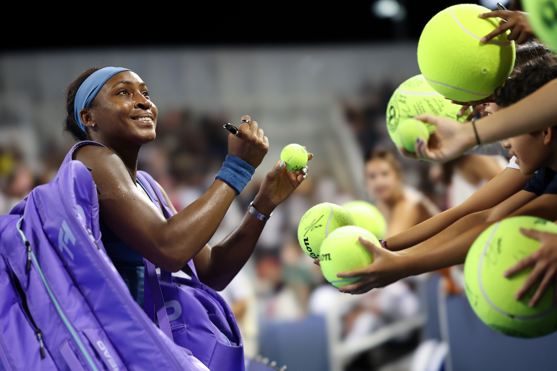 WTA player smiles as she looks up at fans while signing tennis balls