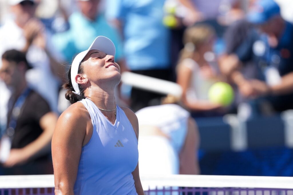 Jessica Pegula looks up at the sky wearing a lavender top and white visor
