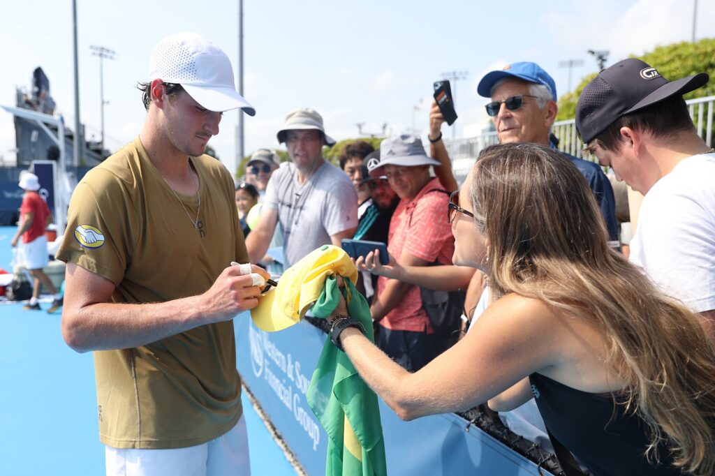 Fonseca signs autographs for the fans wearing a brown shirt and white cap
