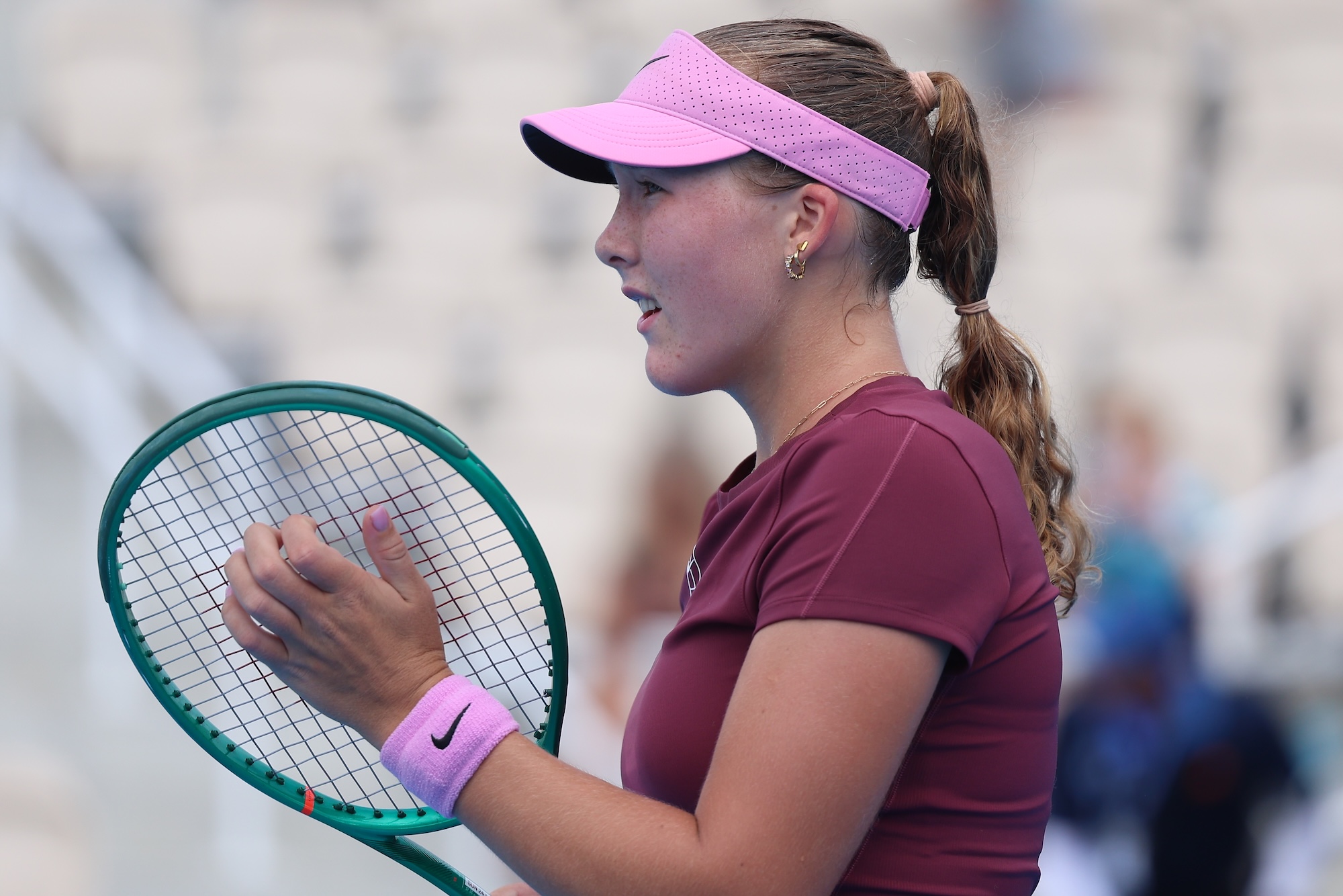 Mirra Andreeva grips her racquet wearing a pink visor