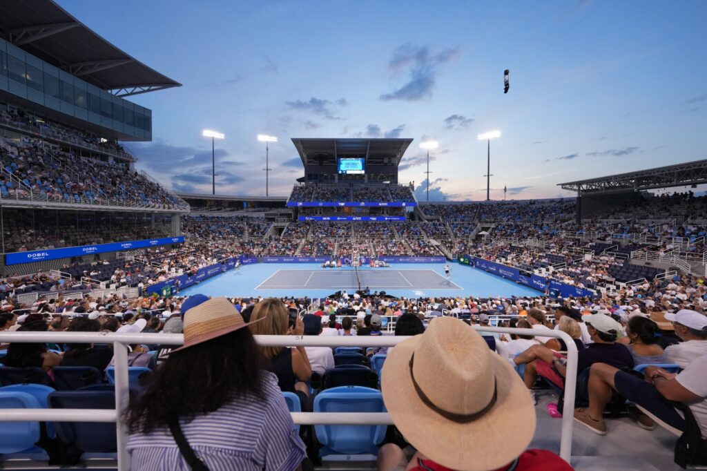A wide view of a stadium court at dusk, a in a straw hat in the foreground.