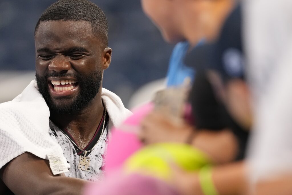 Frances Tiafoe laughs courtside with a towel around his neck, wearing a chain with a Big Foe pendant.
