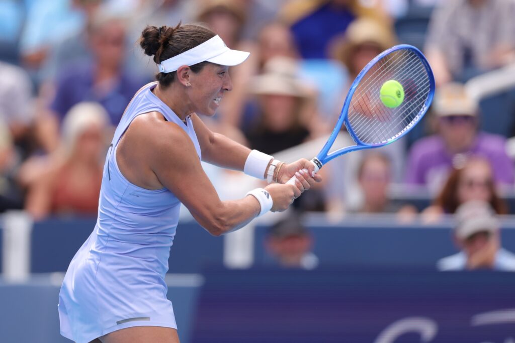 Pegula hits the ball wearing a lavendar tennis dress and white visor