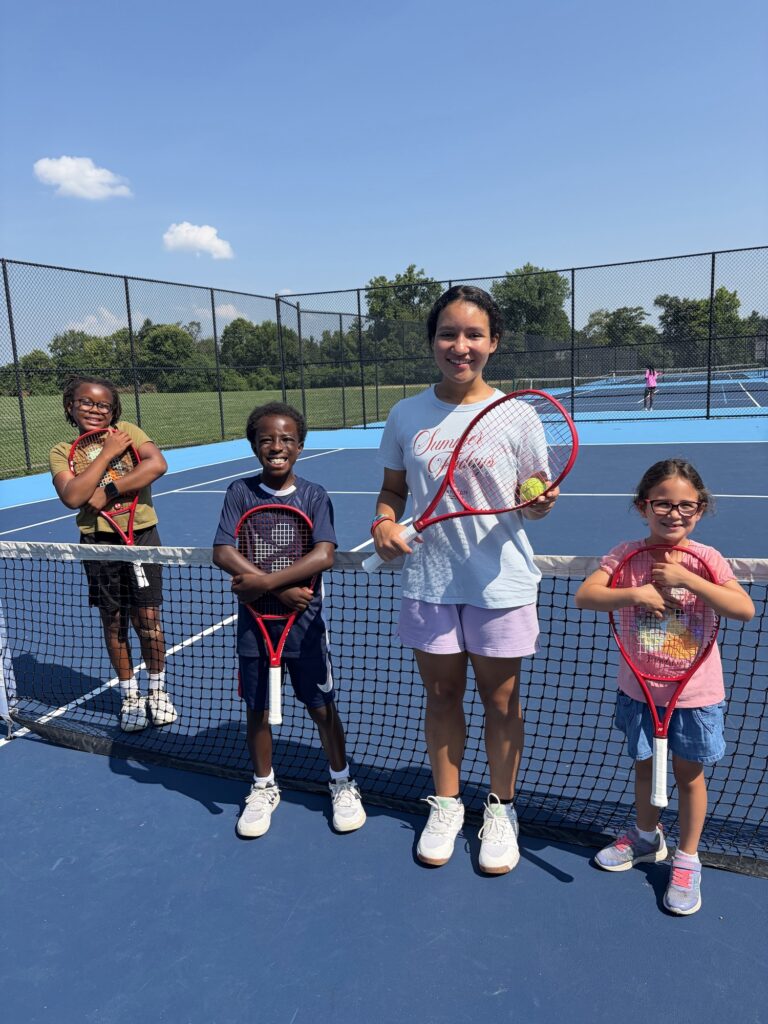 Four kids pose on a tennis court