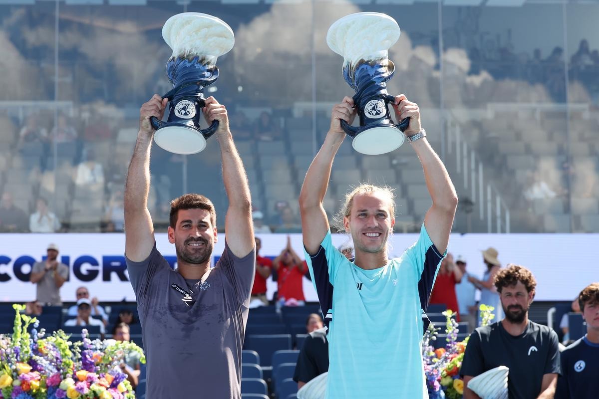 ATP doubles winners smile and pose on court holding their trophies above their heads
