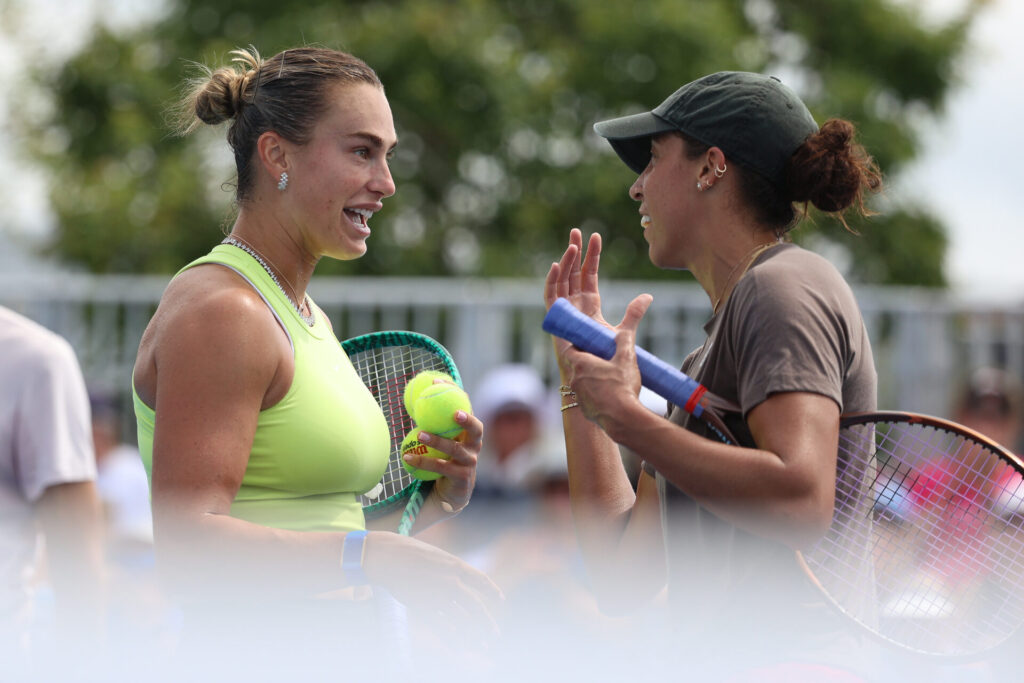 Jessica Pegula talking and smiling on a tennis court, each holding a tennis racket