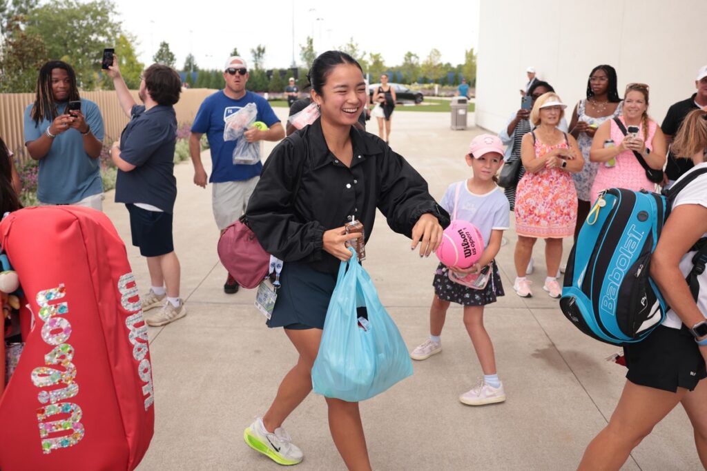 A tennis player in black greets fans