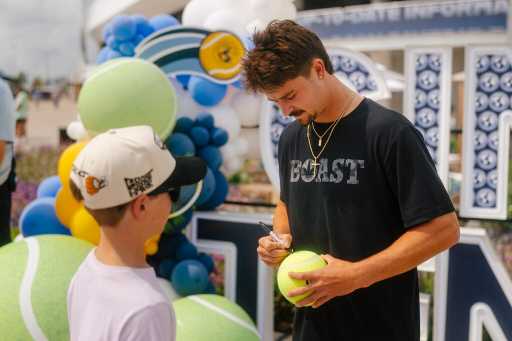 J.J. Wolf signs a tennis ball for a fan