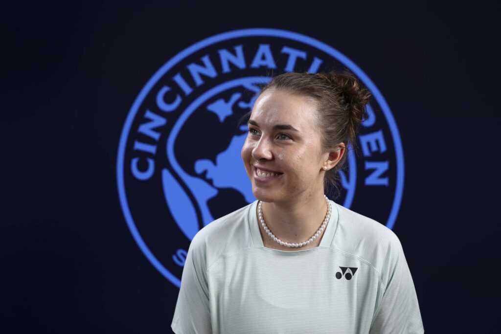 Linda Noskova smiles while wearing a light sports shirt and a pearl necklace, with the Cincinnati Open logo in the background.